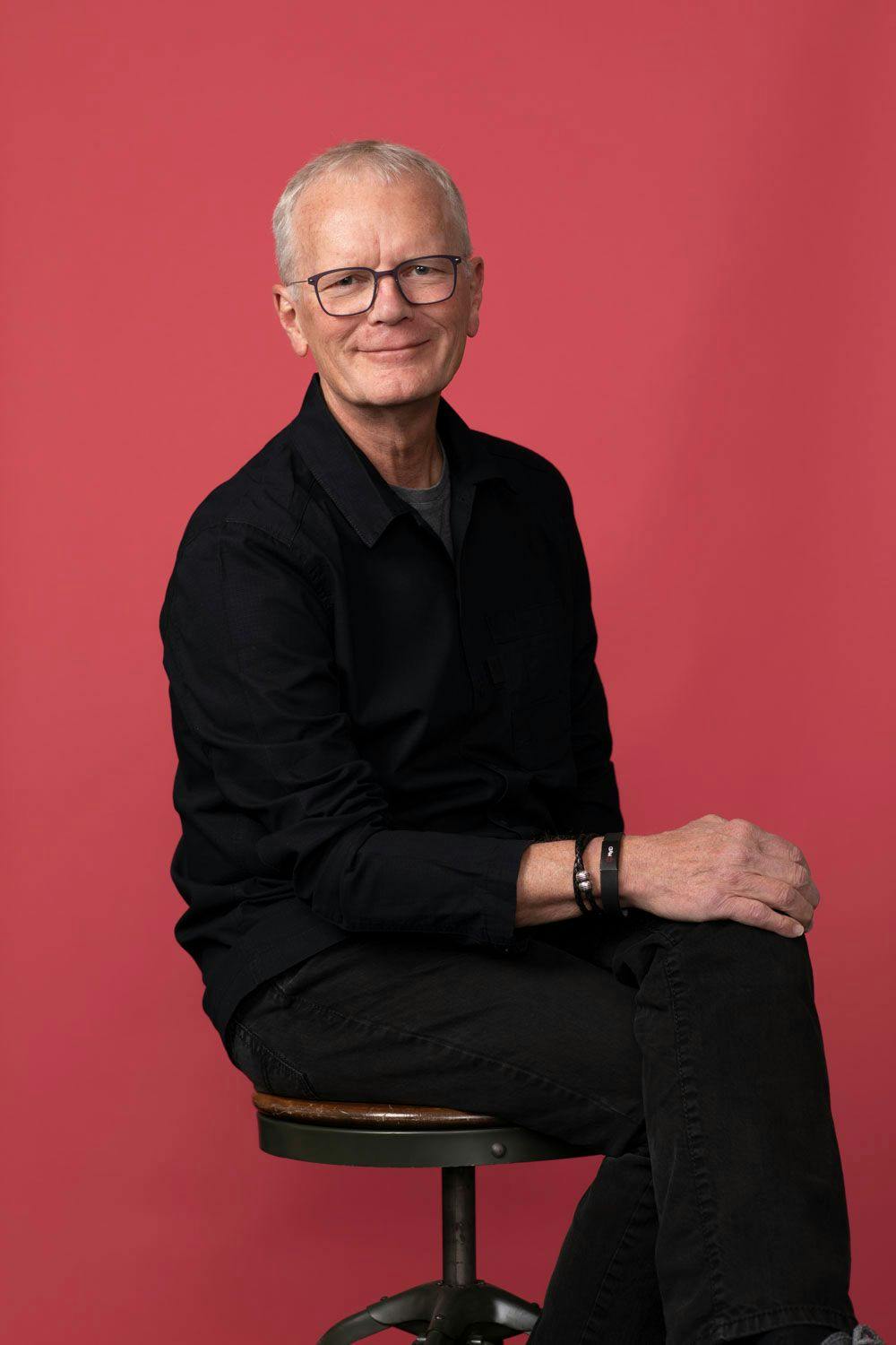 Richard Shear sitting on a stool against a red backdrop.