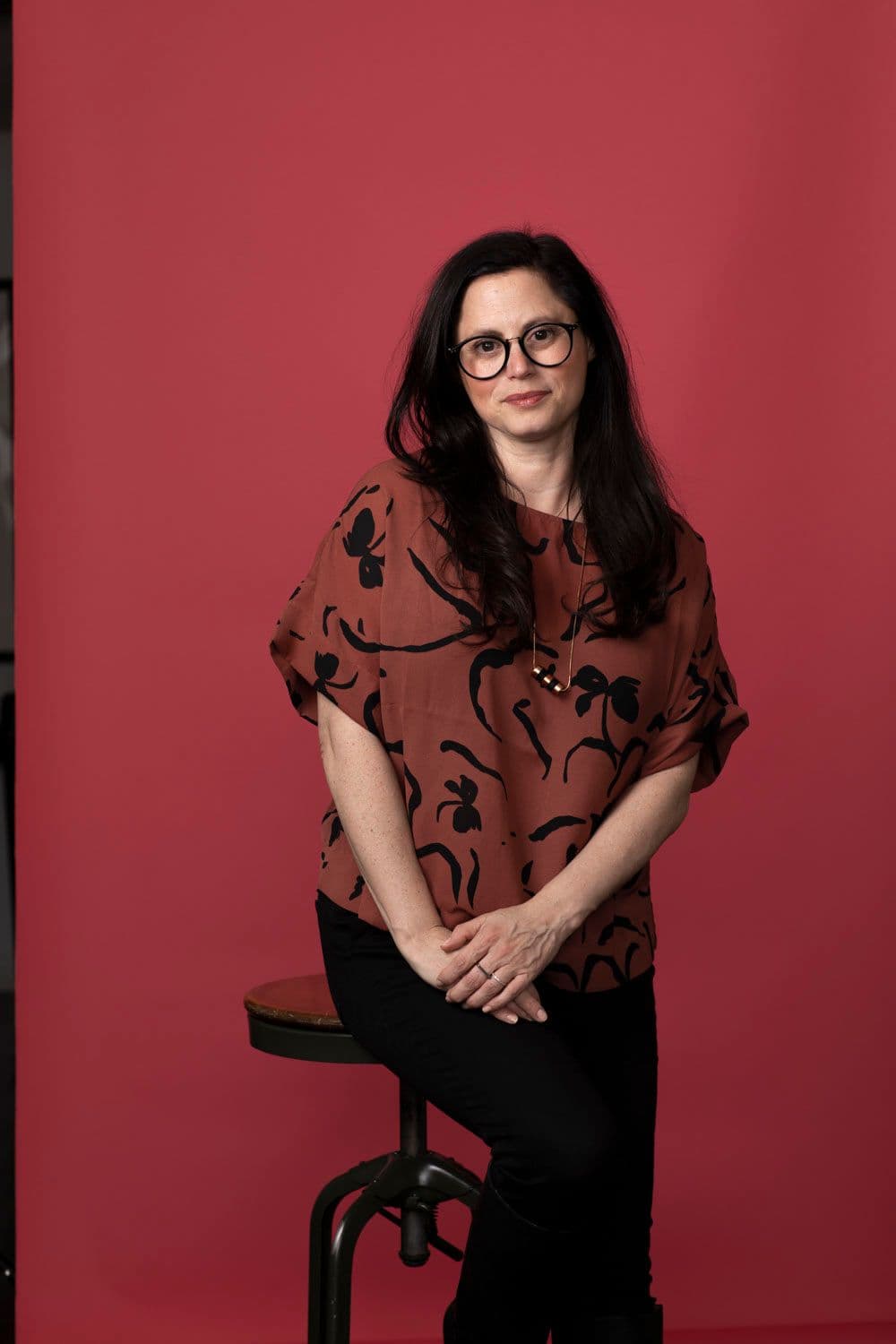 Melanie Wiesenthal sitting on a stool against a red backdrop.