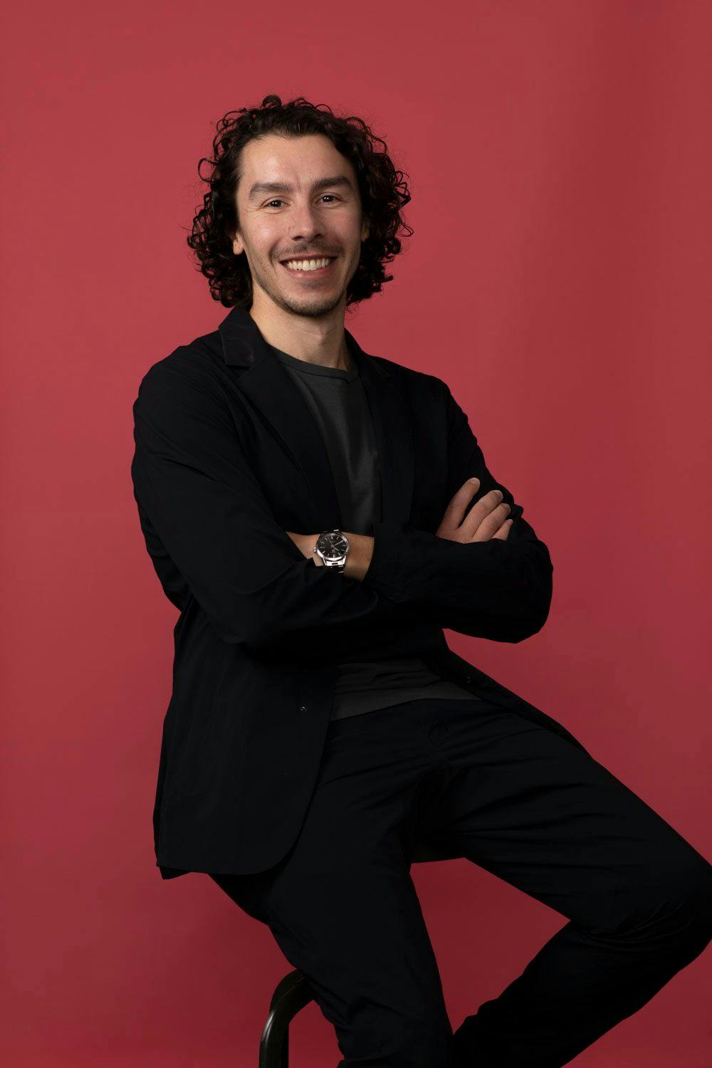 Pablo Ulpiano sitting on a stool against a red backdrop.