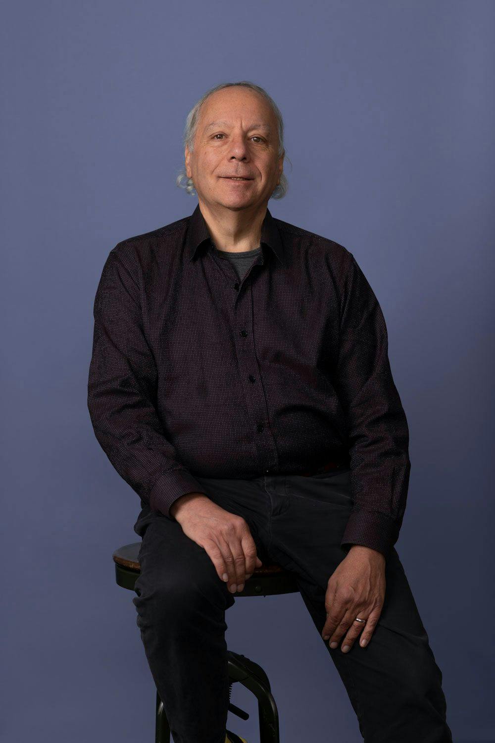 Dr. Dan Formosa sitting on a stool against a purple backdrop.