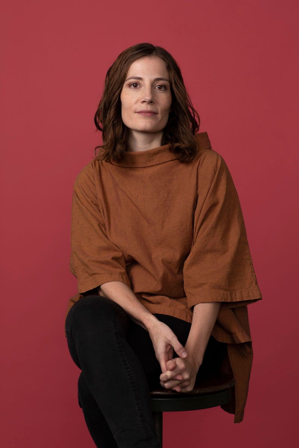 Gena Cuba sitting on a stool against a red backdrop.