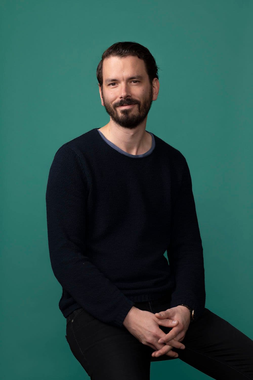Andrew Miller sitting on a stool against a green backdrop.